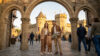 Une famille souriante avec une carte devant l'entrée en pierre d'un château médiéval au Puy du Fou.